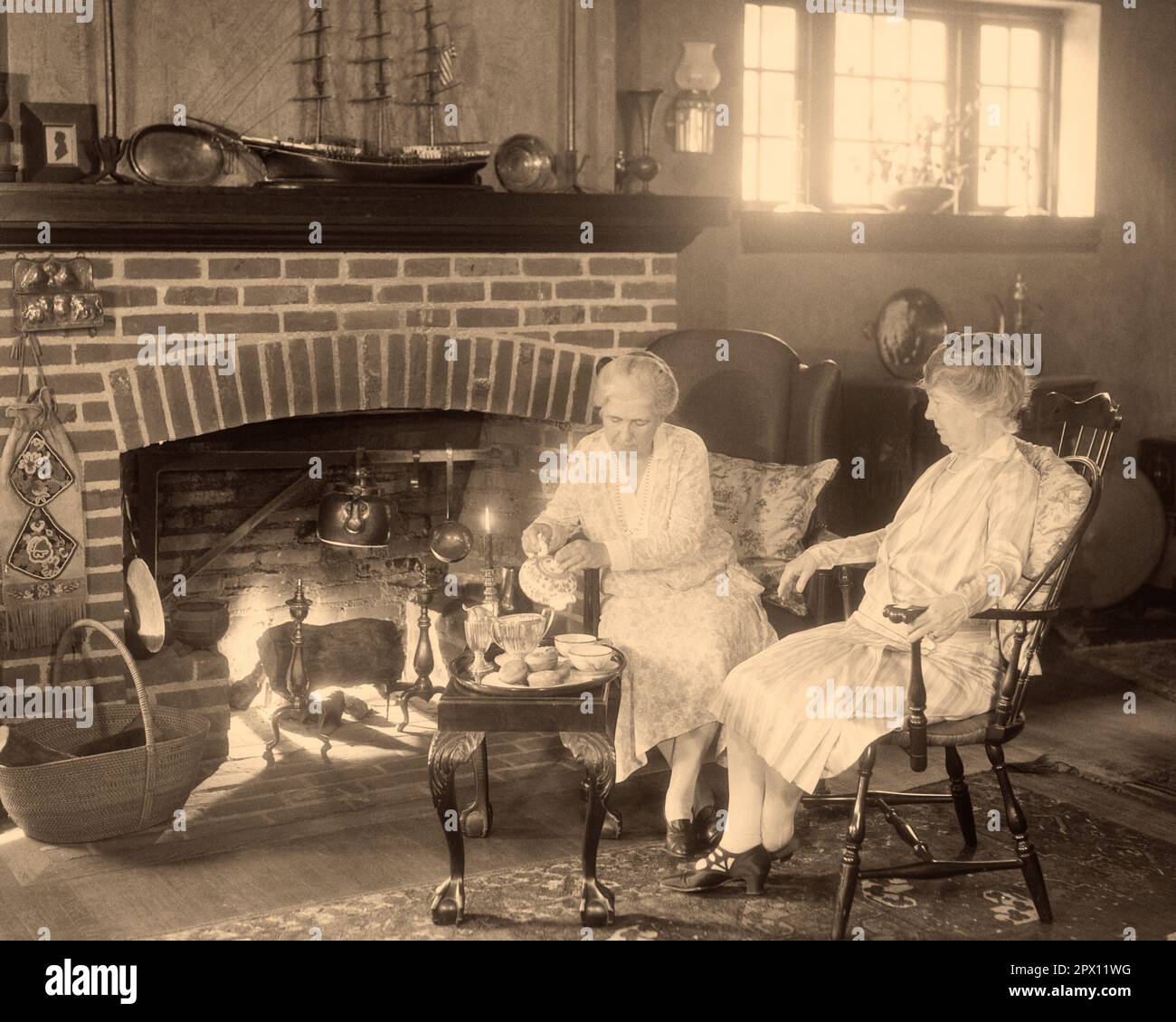 1930s TWO SENIOR GRANDMOTHERS SITTING TOGETHER BY FIREPLACE ONE POURING TEA FOR THE OTHER - m3115 HAR001 HARS HOME LIFE COPY SPACE FRIENDSHIP FULL-LENGTH LADIES PERSONS INSPIRATION SENIOR ADULT B&W SENIOR WOMAN DECORATION DECOR OLD AGE OLDSTERS OLDSTER INTERIORS GRANDMOTHERS ELDERS FRIENDLY INTERIOR DESIGN TEA TIME TEAPOT ELDERLY WOMAN HOME DECOR RELAXATION TOGETHERNESS BLACK AND WHITE CAUCASIAN ETHNICITY FURNISHINGS HAR001 OLD FASHIONED Stock Photo
