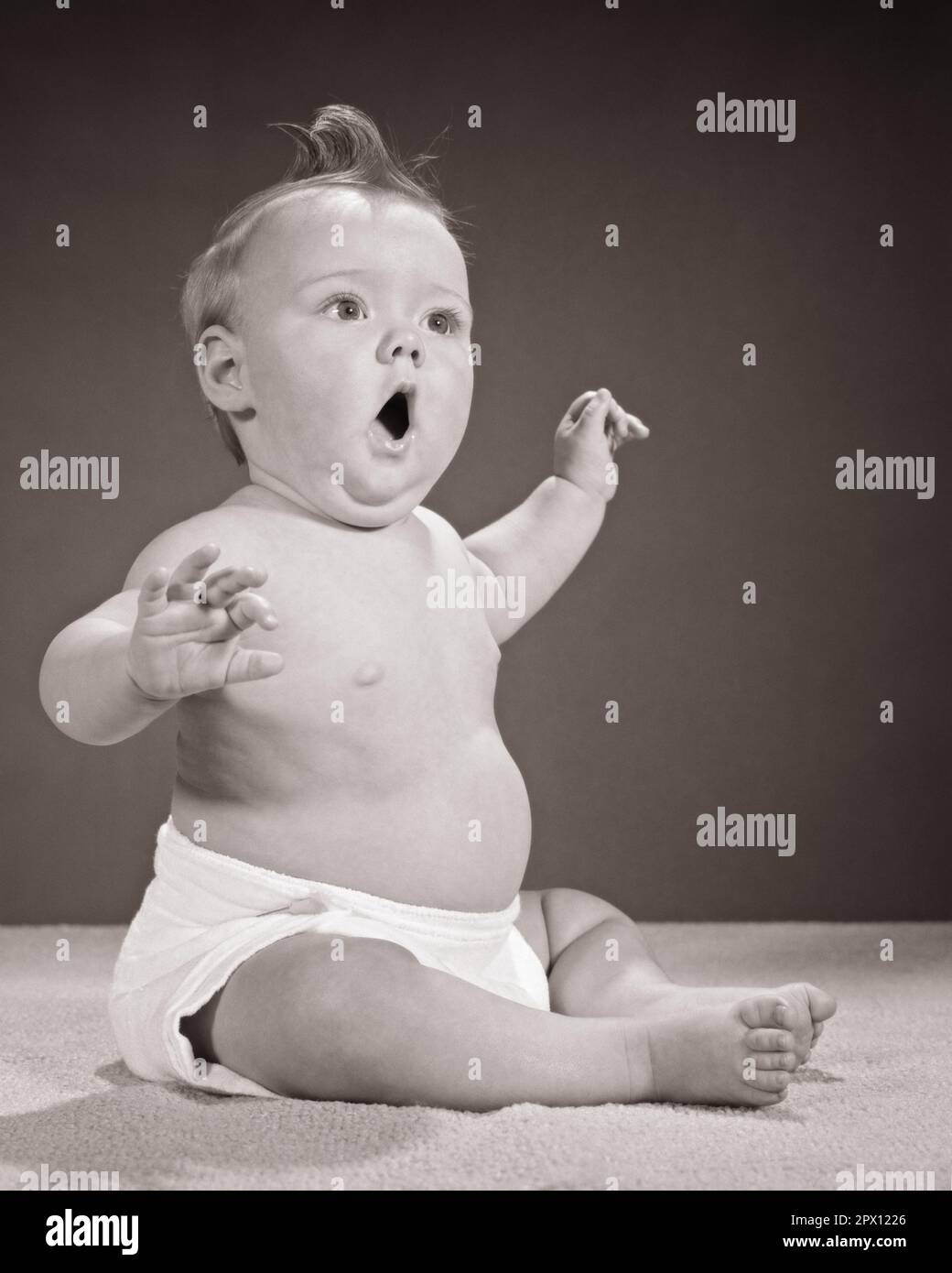 1960s CHUBBY BABY SITTING UP ARMS RAISED LOOK OF SURPRISE FACIAL