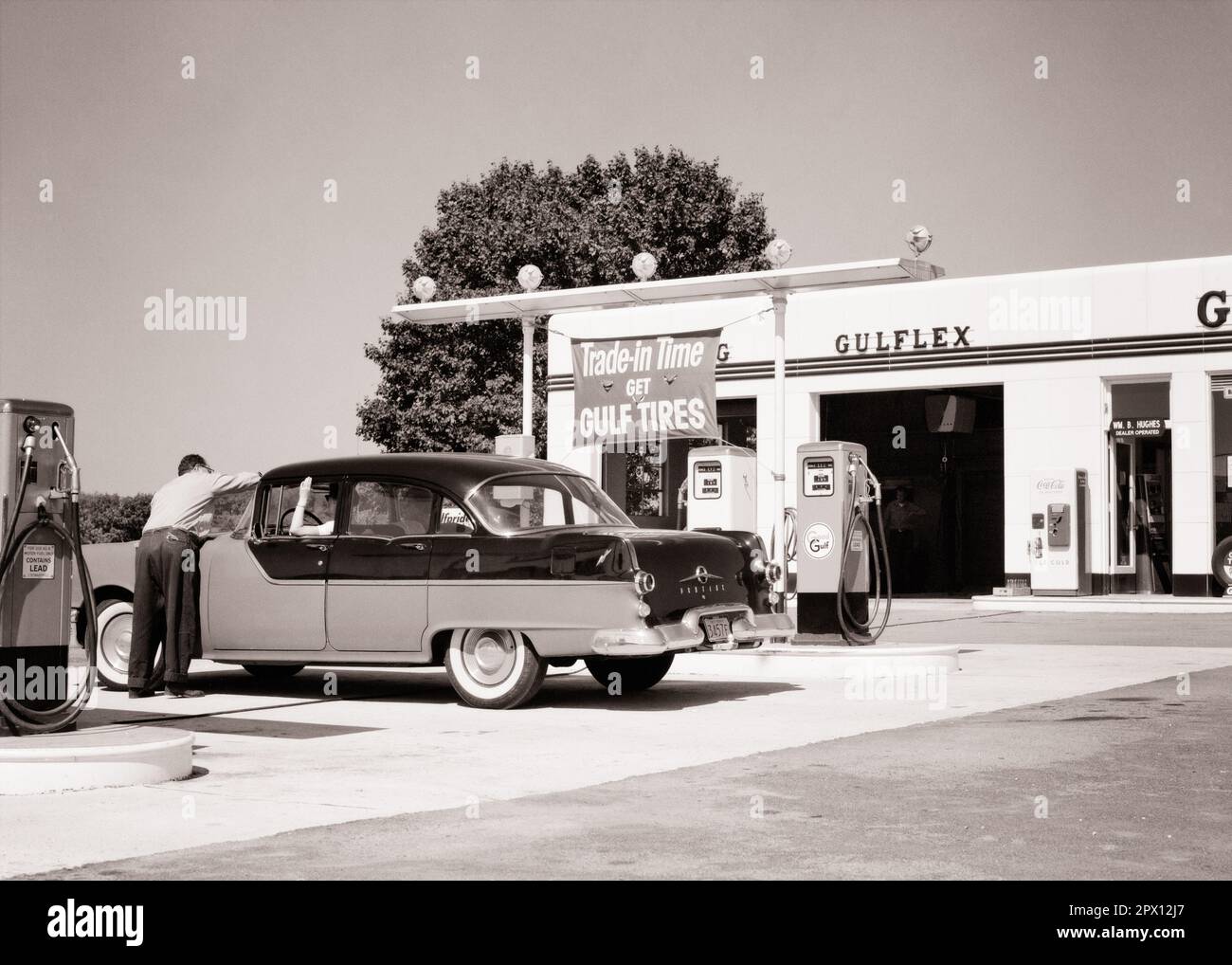 1950s ANONYMOUS MAN GULF GAS STATION ATTENDANT CLEANING WINDSHIELD FOR WOMAN DRIVING 1955 FOUR DOOR PONTIAC SEDAN AUTOMOBILE - m399 HAR001 HARS GULF LIFESTYLE SATISFACTION FEMALES JOBS COPY SPACE HALF-LENGTH LADIES PERSONS AUTOMOBILE MALES FUEL TRANSPORTATION B&W PUMPS SKILL OCCUPATION SKILLS GAS STATION CUSTOMER SERVICE SEDAN AUTOS SERVICE STATION LABOR EMPLOYMENT OCCUPATIONS GASOLINE CONCEPTUAL PONTIAC AUTOMOBILES VEHICLES WINDSHIELD EMPLOYEE ATTENDANT COOPERATION PETROL PETROLEUM TIRES 1955 BLACK AND WHITE CAUCASIAN ETHNICITY HAR001 LABORING OLD FASHIONED Stock Photo