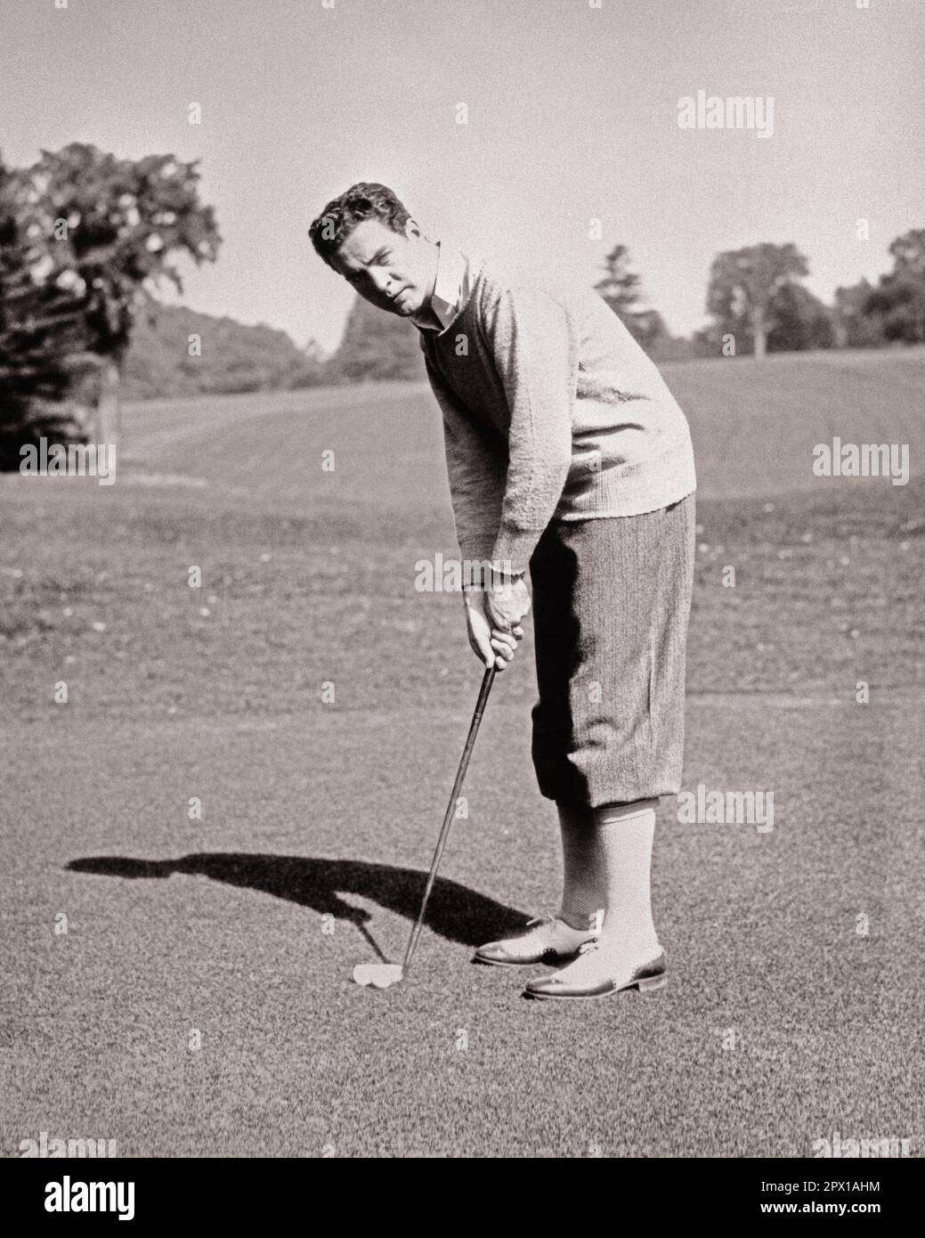 1920s MAN GOLFER ON PUTTING GREEN LOOKING AT CAMERA WEARING SWEATER PLUS FOURS AND TWO TONE SPECTATOR BROGUE STYLE GOLFING SHOES - g3644 HAR001 HARS SATISFACTION COPY SPACE FULL-LENGTH PERSONS MALES GOLFING ATHLETIC CONFIDENCE B&W EYE CONTACT ACTIVITY PHYSICAL WELLNESS ADVENTURE GOLFERS LEISURE STRENGTH STYLES AND CHOICE EXCITEMENT RECREATION HANDSOME ON CONNECTION FLEXIBILITY LINKS MUSCLES SPECTATOR STYLISH PLUS FOURS TWO-TONE FASHIONS FOCUSED MID-ADULT MID-ADULT MAN PRECISION YOUNG ADULT MAN BLACK AND WHITE CAUCASIAN ETHNICITY CONCENTRATING HAR001 OLD FASHIONED Stock Photo