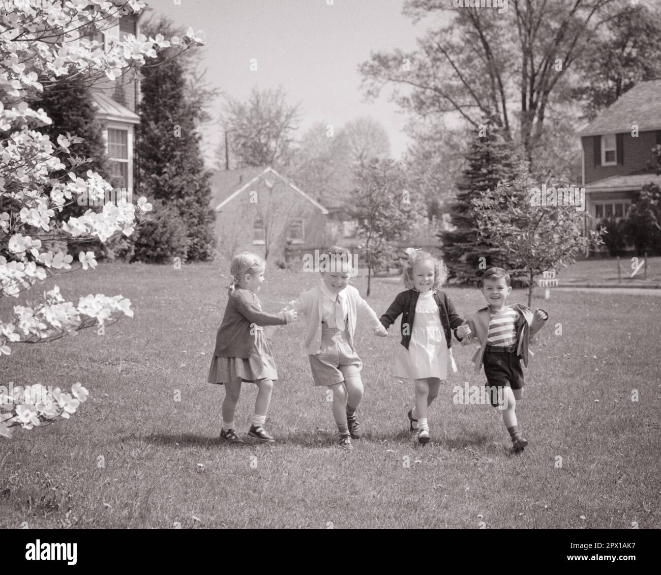 1940s 1950s TWO BOYS TWO GIRLS BROTHERS AND SISTERS RUNNING TOGETHER HOLDING HANDS IN SPRINGTIME ON FRONT LAWN OF SUBURBAN HOME - j1314 HAR001 HARS JUVENILE YARD STYLE LAUGH TEAMWORK PLEASED JOY LIFESTYLE SATISFACTION FEMALES EASTER BROTHERS HEALTHINESS HOME LIFE COPY SPACE FRIENDSHIP FULL-LENGTH MALES SIBLINGS SISTERS B&W NEIGHBORS FREEDOM HAPPINESS NEIGHBORHOOD CHEERFUL ADVENTURE LEISURE BLOSSOM AND EXCITEMENT RECREATION SIBLING SMILES SWEATERS CONNECTION JOYFUL STYLISH SUPPORT FANCY DRESS COOPERATION GROWTH JUVENILES SPRING SEASON SPRINGTIME TOGETHERNESS BLACK AND WHITE CAUCASIAN ETHNICITY Stock Photo