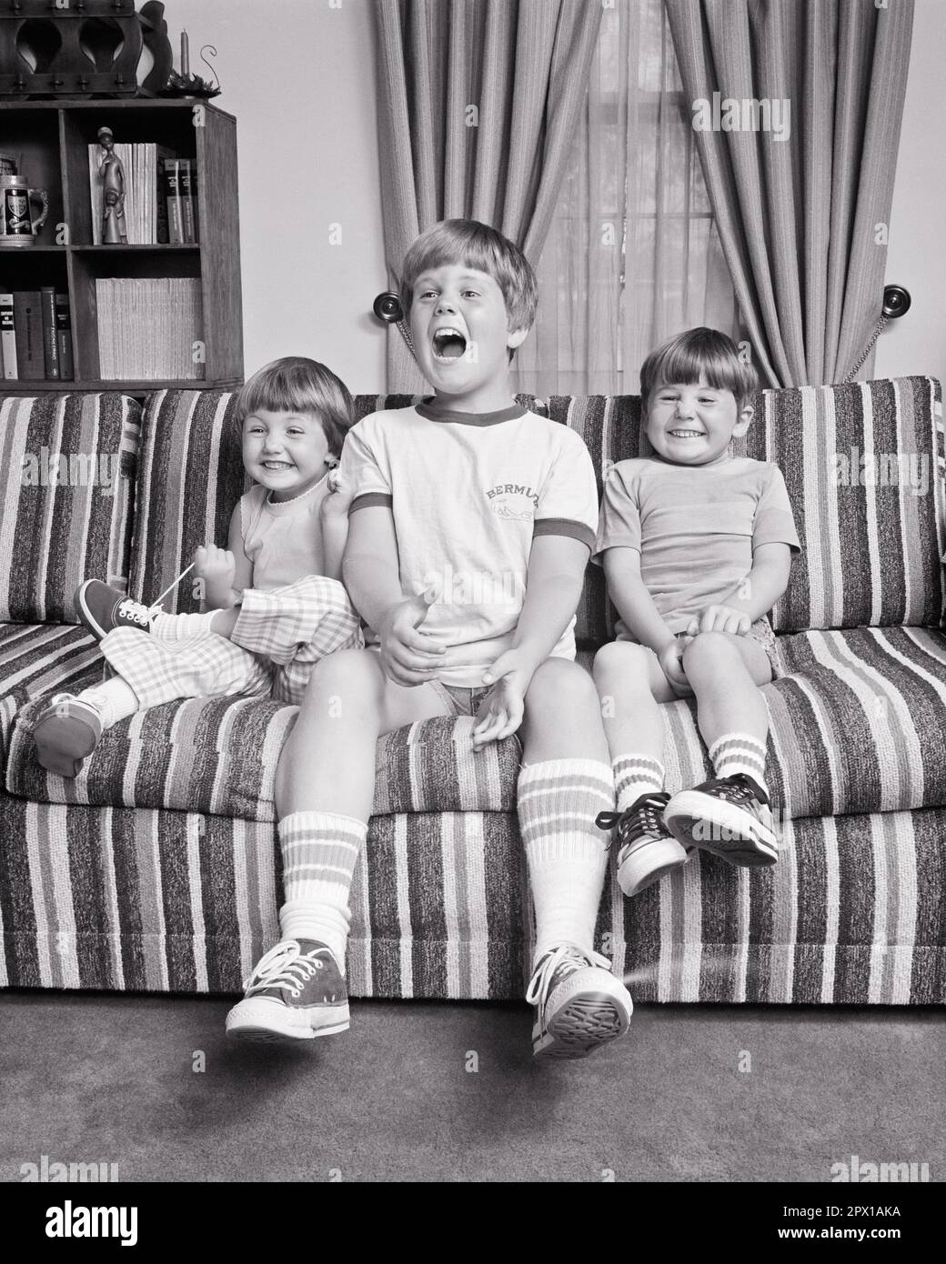 1970s THREE KIDS 2 BOYS 1 GIRL SIBLING BROTHERS SISTER SITTING ON STRIPED COUCH MAKING FACES LAUGHING SMILING  - j13869 HAR001 HARS DESIGN PLEASED FAMILIES JOY LIFESTYLE STRIPED BROTHERS HEALTHINESS HOME LIFE COPY SPACE FRIENDSHIP FULL-LENGTH STRIPES ENTERTAINMENT SIBLINGS SISTERS B&W TELEVISIONS DECORATION DECOR HUMOROUS HAPPINESS CHEERFUL BROADCASTING DISCOVERY EXCITEMENT INTERIORS COMICAL SIBLING CONNECTION LITTLE SISTER CONCEPTUAL COMEDY HAIRSTYLES INTERIOR DESIGN JOYFUL COOPERATION FAMILY RESEMBLANCE GROWTH HOME DECOR PRE-TEEN PRE-TEEN GIRL TOGETHERNESS BIG BROTHER BLACK AND WHITE Stock Photo