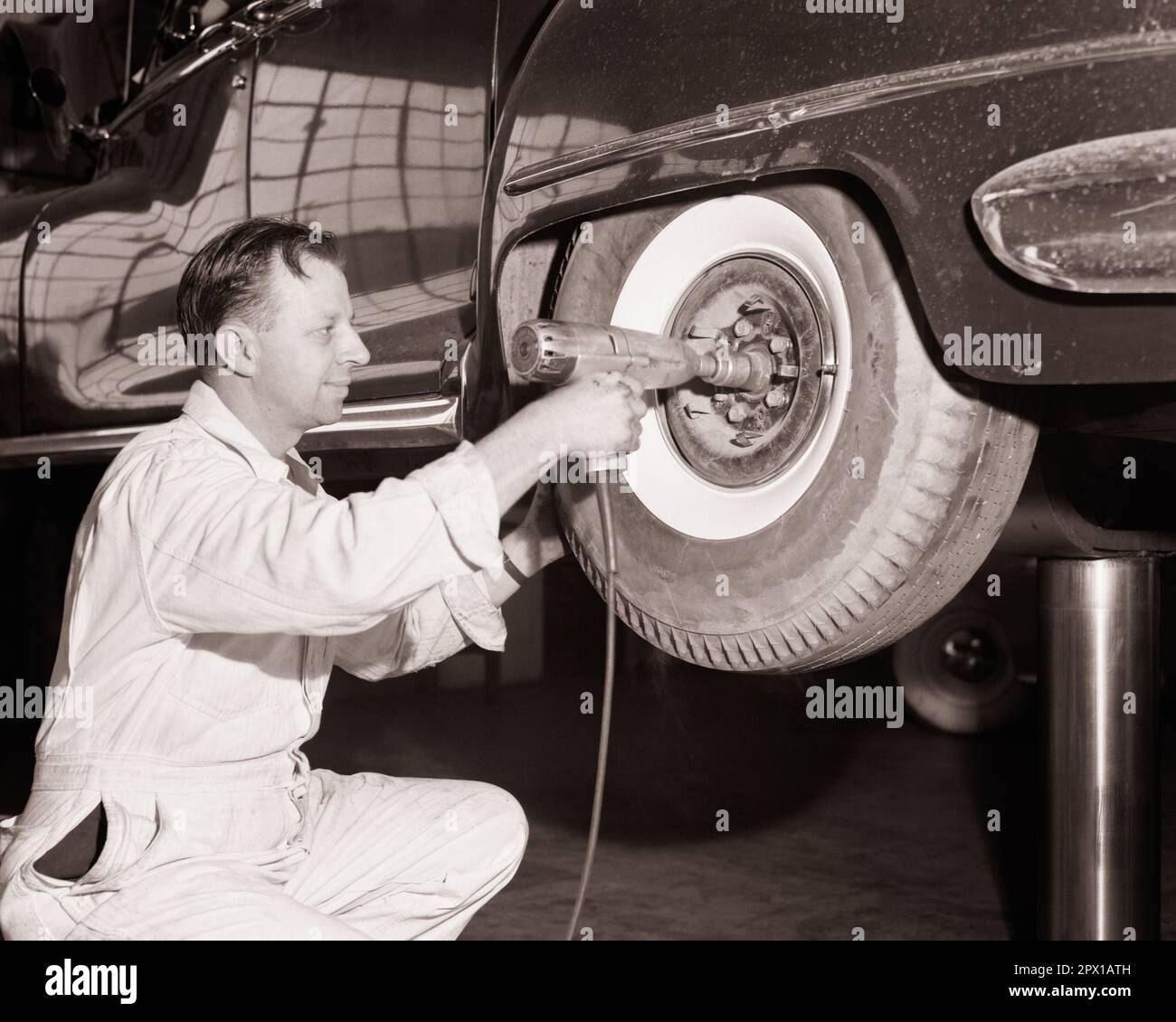 1950s GARAGE MECHANIC USING AN ELECTRIC WRENCH ON WHEEL TIRE HUB NUT - m3187 PRC001 HARS PROFESSION CONFIDENCE TRANSPORTATION B&W CARRIAGE SKILL OCCUPATION SKILLS CUSTOMER SERVICE AUTOS SERVICE STATION WHITEWALL CAREERS LOW ANGLE POWERFUL LABOR MECHANICS EMPLOYMENT NEAR OCCUPATIONS USING REPAIRING WRENCH AUTOMOBILES VEHICLES INFRASTRUCTURE EMPLOYEE HUB MID-ADULT MID-ADULT MAN NUT SERVICING BLACK AND WHITE CAUCASIAN ETHNICITY LABORING OLD FASHIONED Stock Photo