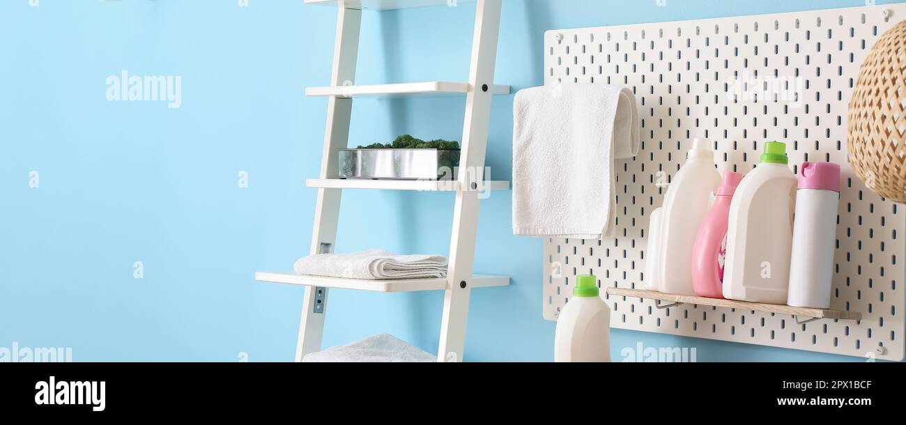 Pegboard with bottles of detergents and rack with towels near blue wall