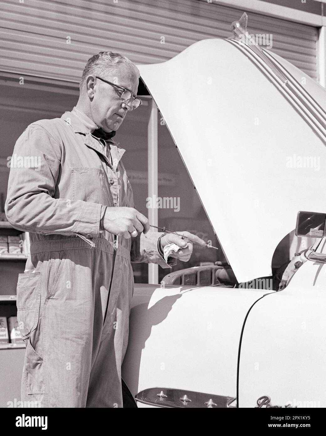 1950s MAN GAS STATION ATTENDANT CHECKING LEVEL OF OIL IN AUTOMOBILE ENGINE - m5124 HAR001 HARS PERSONS OVERALLS AUTOMOBILE MALES PROFESSION TRANSPORTATION MIDDLE-AGED B&W GOALS SKILL OCCUPATION SKILLS MIDDLE-AGED WOMAN DISCOVERY PROTECTION CUSTOMER SERVICE AUTOS CAREERS LOW ANGLE LABOR OPPORTUNITY EMPLOYMENT OCCUPATIONS MAINTENANCE AUTOMOBILES INSPECTING VEHICLES INFRASTRUCTURE OILS EMPLOYEE ATTENDANT DIPSTICK LEVEL LUBRICATION BLACK AND WHITE CAUCASIAN ETHNICITY COVERALLS FOSSIL FUEL HAR001 LABORING OLD FASHIONED Stock Photo