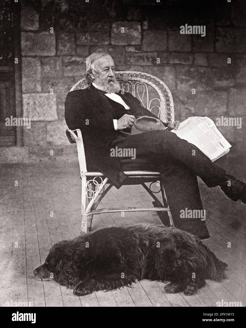 1870s ELDERLY BEARDED MAN SITTING IN WICKER CHAIR ON PORCH OF STONE HOUSE HOLDING A NEWSPAPER A BLACK DOG LYING AT HIS FEET - o3789 HAR001 HARS LIFESTYLE ELDER HOME LIFE COPY SPACE FULL-LENGTH PERSONS WICKER MALES RETIREMENT MIDDLE-AGED 1800s B&W MIDDLE-AGED MAN RETIREE MAMMALS OLD AGE OLDSTERS OLDSTER HIS LEISURE CANINES EXTERIOR FACIAL HAIR ELDERS POOCH 1870s BEARDED BEARDS CANINE MAMMAL RELAXATION BLACK AND WHITE CAUCASIAN ETHNICITY HAR001 OLD FASHIONED Stock Photo