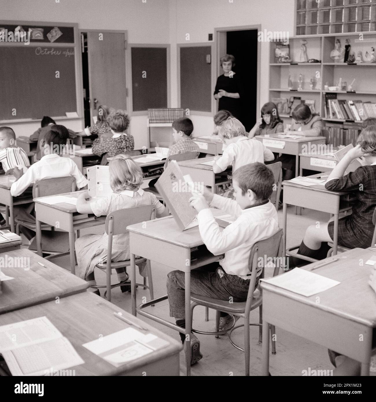 1960s TEACHER STANDING IN DOORWAY TO CLASSROOM MONITORING STUDENTS READING AND STUDYING AT THEIR DESKS - s15909 HAR001 HARS COPY SPACE HALF-LENGTH LADIES PERSONS MALES MIDDLE-AGED B&W DESKS SCHOOLS GRADE MIDDLE-AGED WOMAN HIGH ANGLE AFRICAN-AMERICANS AFRICAN-AMERICAN AND INSTRUCTOR BLACK ETHNICITY REAR VIEW OCCUPATIONS PRIMARY FROM BEHIND EDUCATOR MONITORING BACK VIEW EDUCATING EDUCATORS GRADE SCHOOL INSTRUCTORS MID-ADULT MID-ADULT WOMAN SCHOOL TEACHES BLACK AND WHITE CAUCASIAN ETHNICITY HAR001 OLD FASHIONED AFRICAN AMERICANS Stock Photo
