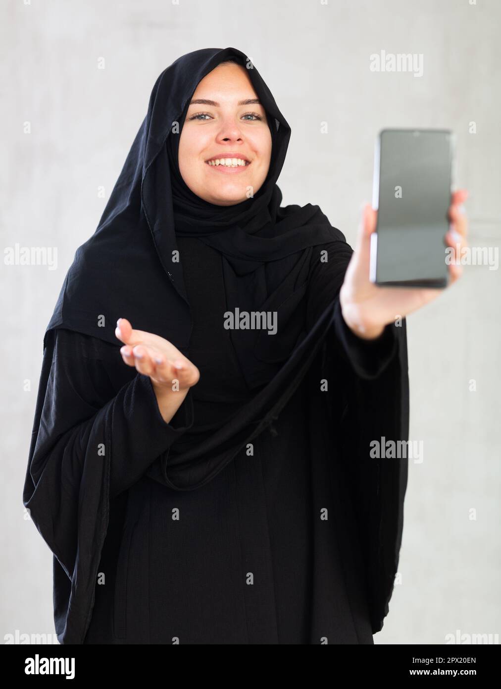 smiling Muslim woman in traditional black hijab shows blank smartphone ...