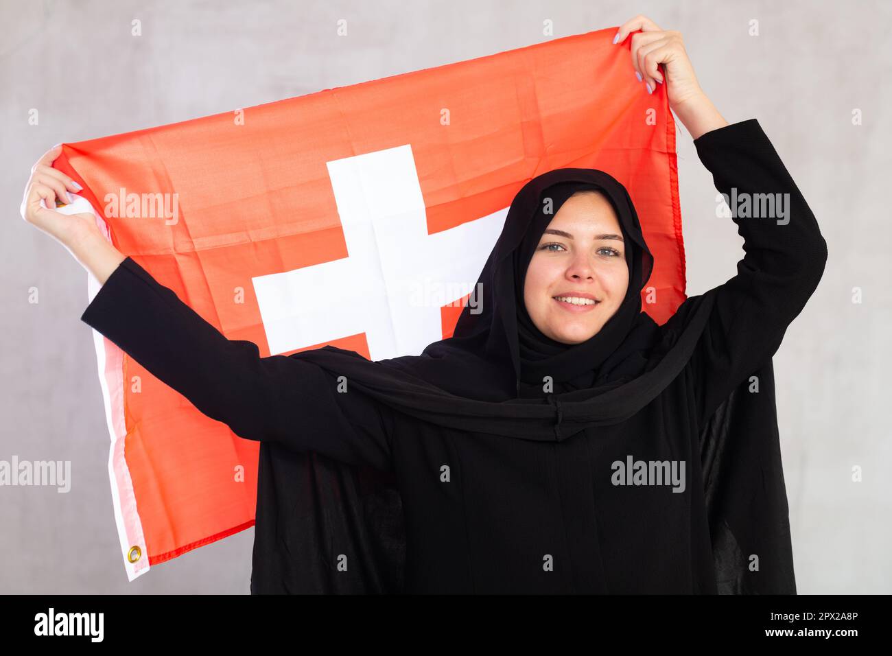 Balanced smiling Muslim woman in traditional black hijab holds flag of