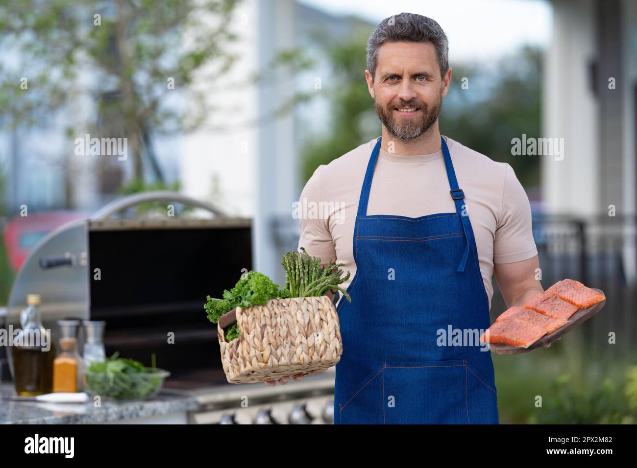 happy barbecue man with salmon in apron. photo of barbecue man with salmon fish. barbecue man with salmon. barbecue man with salmon outdoor. Stock Photo
