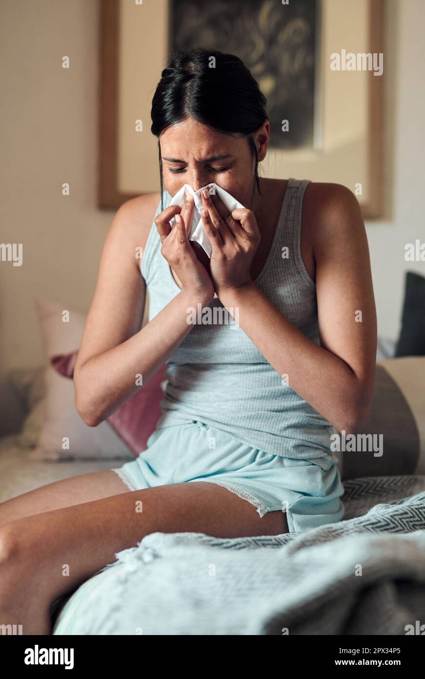No, not the flu...a young woman blowing her nose with a tissue at home Stock Photo