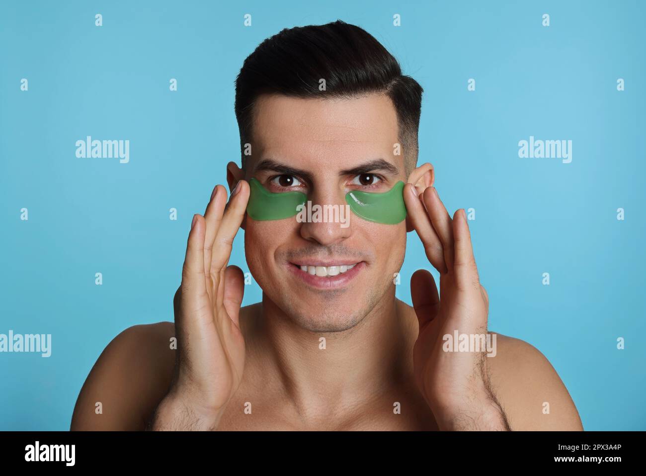 Man applying green under eye patches on light blue background Stock