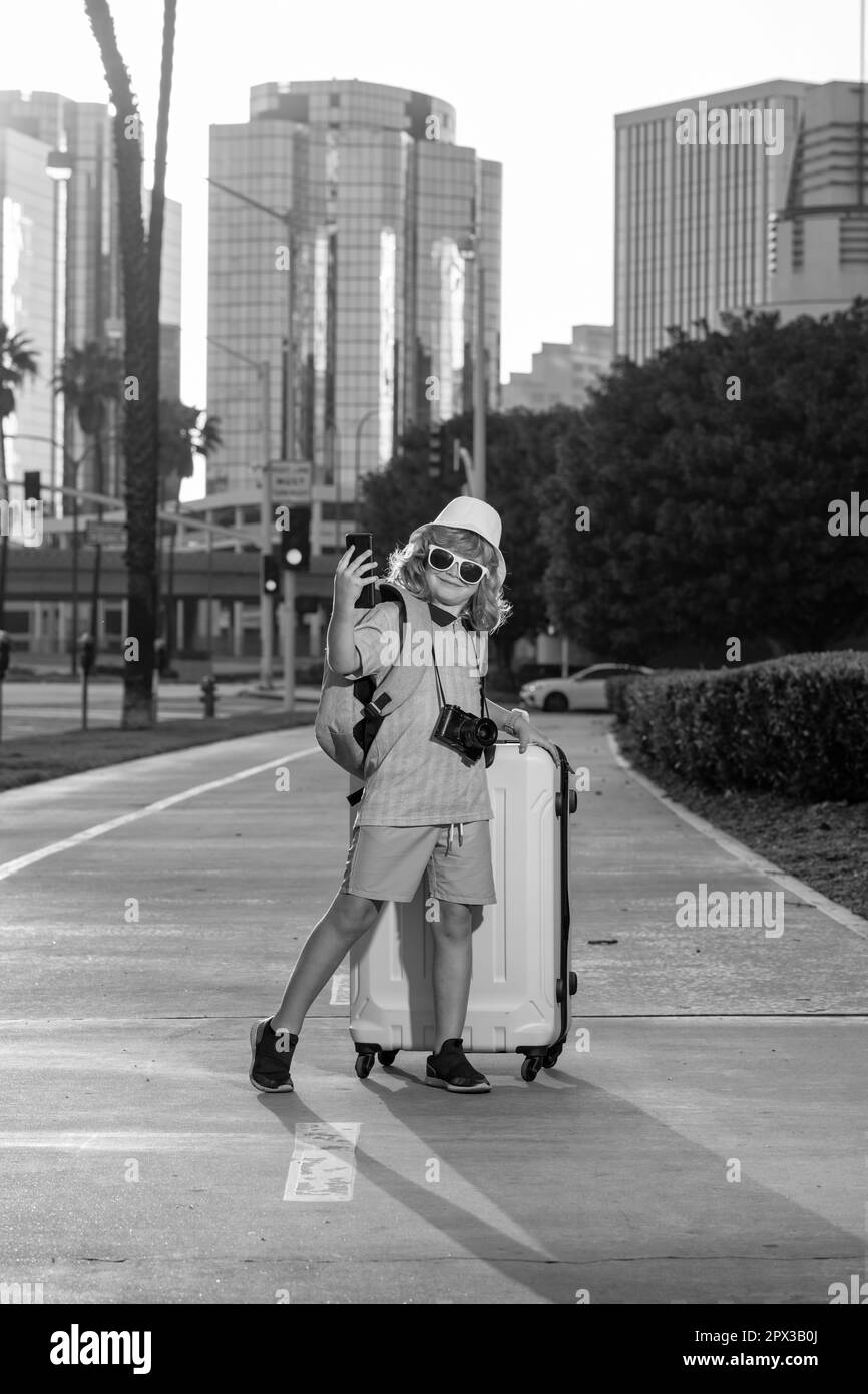 Kid traveller with suitcase going on vacation. Tourist boy on holiday, travel kids concept. Cute boy with suitcase on city street background. Stock Photo