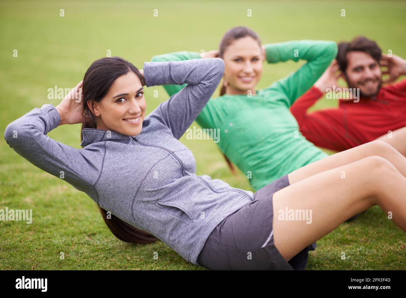 Working out together makes us push ourselves more. Portrait of three friends doing sit-ups together on a sports field. Stock Photo