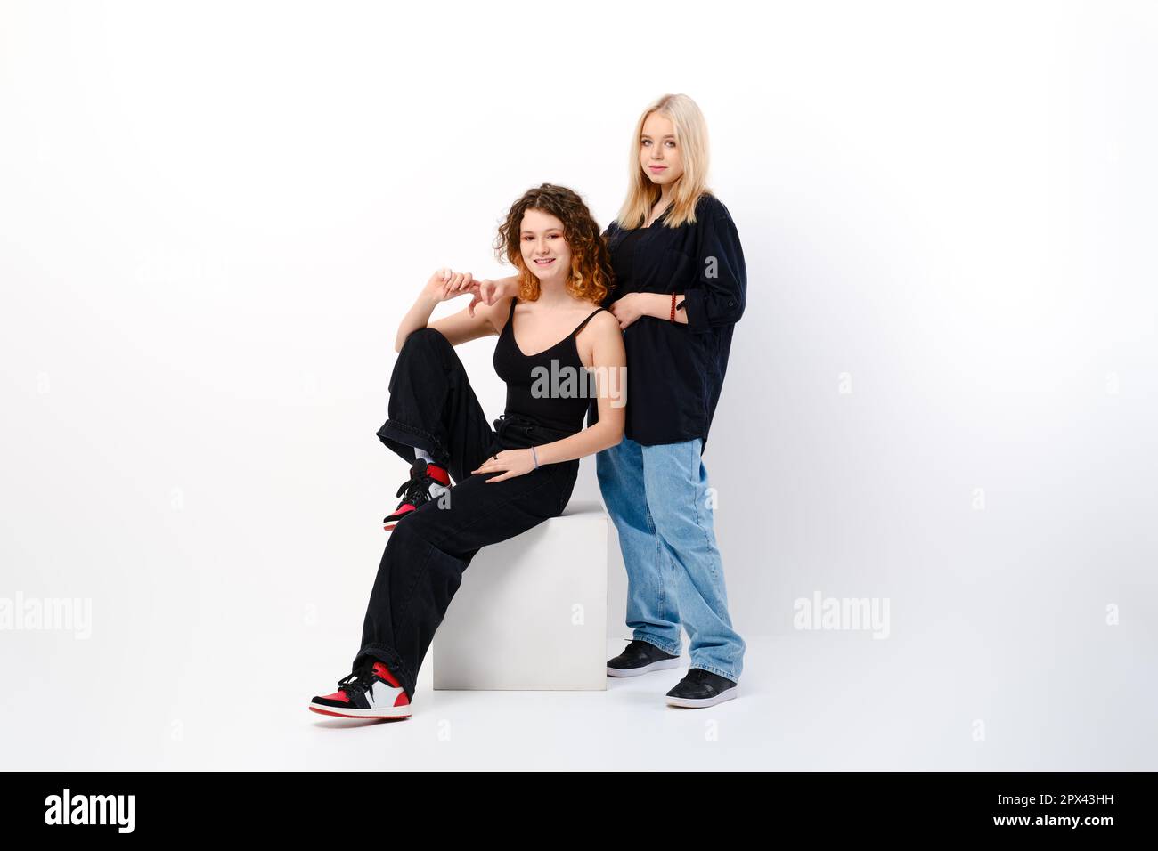 Two positive and funny teen girls together over white studio background Stock Photo