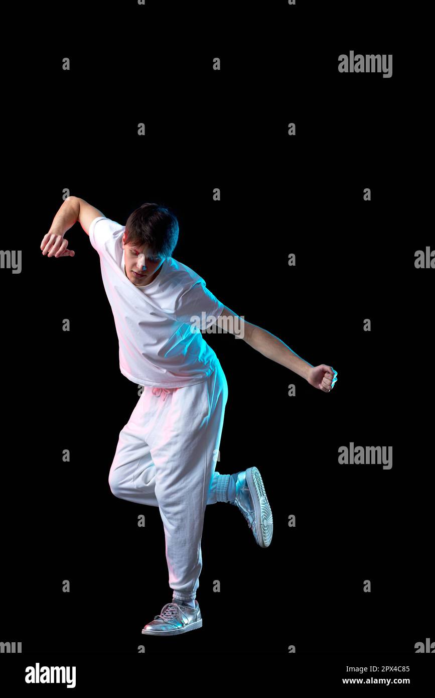 young man in white t-shirt dancing in neon light on black background . Full length Stock Photo