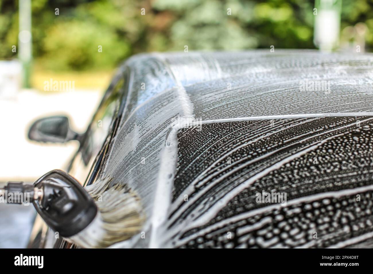 Black dirty car in white soap foam at car wash service station