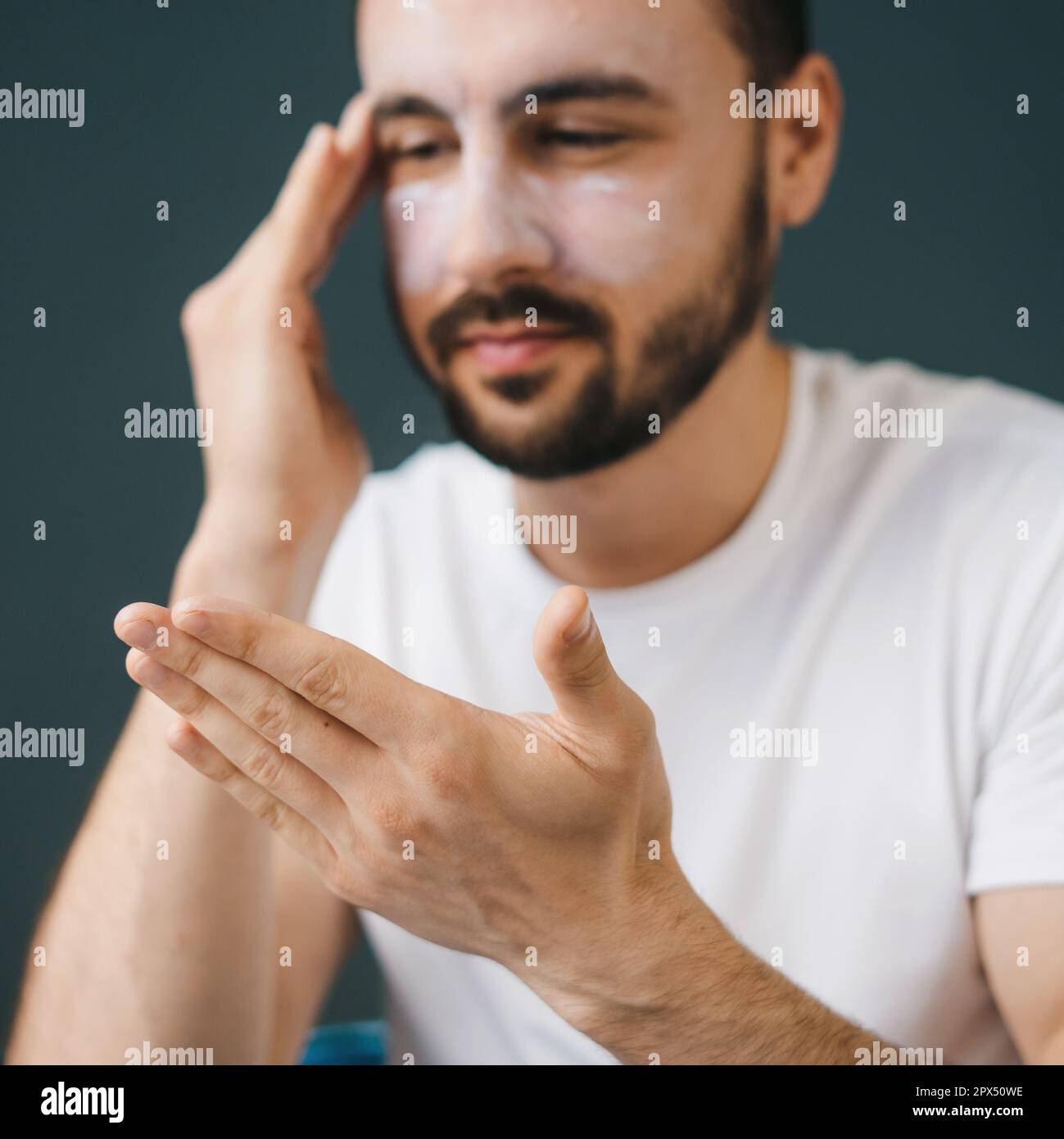 Close-up portrait of a man applying cosmetic clay face mask at home. Male appearance care, relax at home, treat yourself. Stock Photo