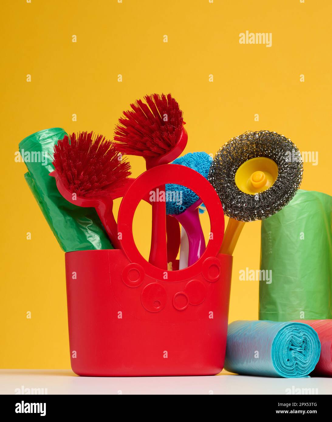 Plastic basket with brushes, disinfectant in a bottle on a yellow background. House cleaning items set Stock Photo