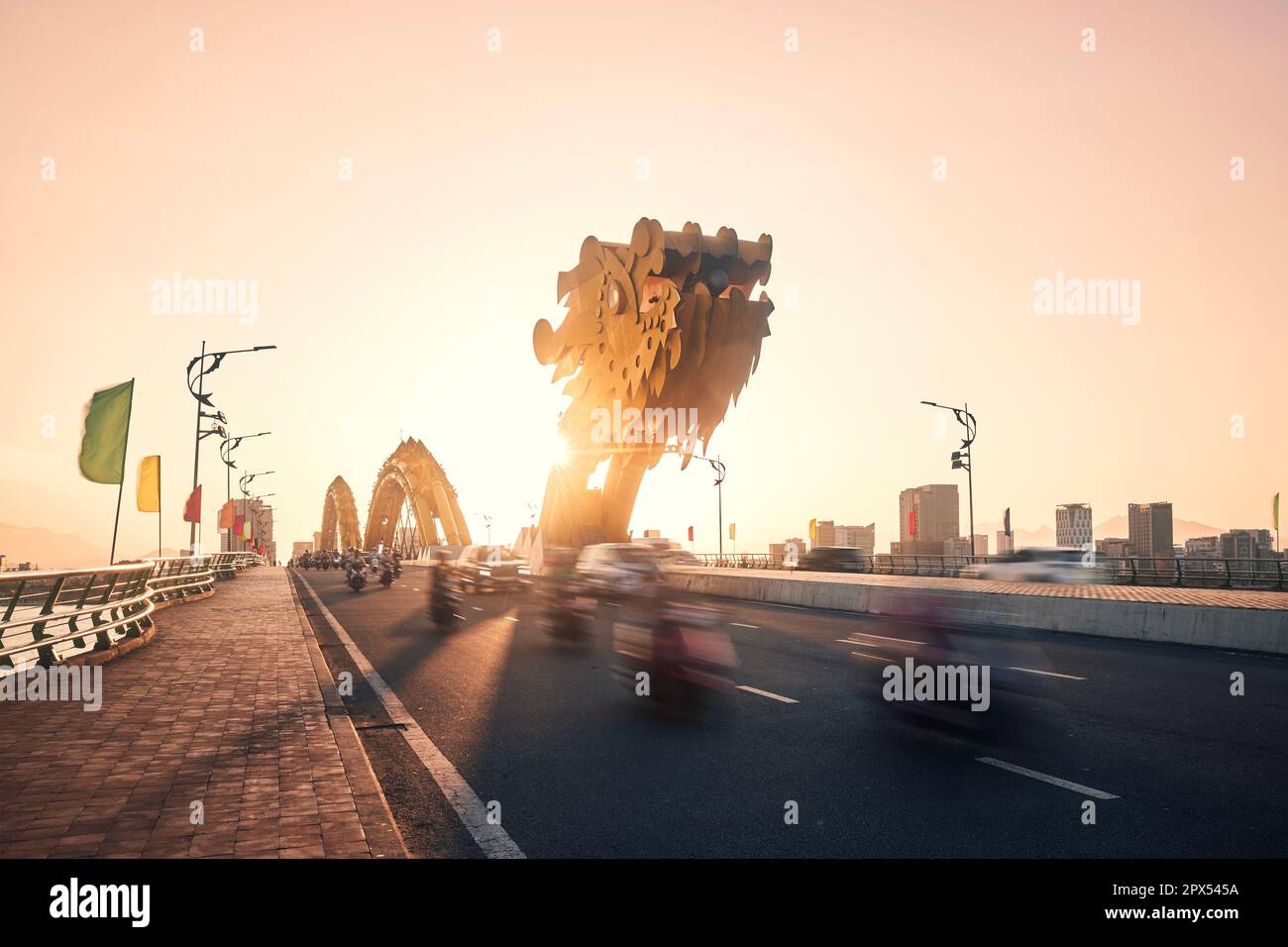 Traffic with a lot of motorcycles in blurred motion on Dragon Bridge. Da Nang city at golden sunset, Vietnam. Stock Photo