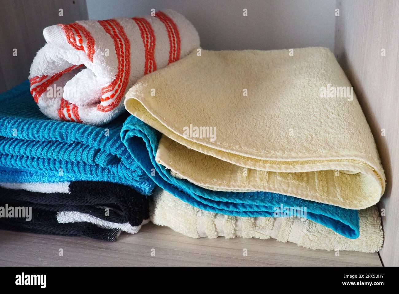 Towels on a shelf in a white cabinet. Clean ironed pink, yellow, blue towels folded in a pile. Organization of household items in the bathroom or clos Stock Photo