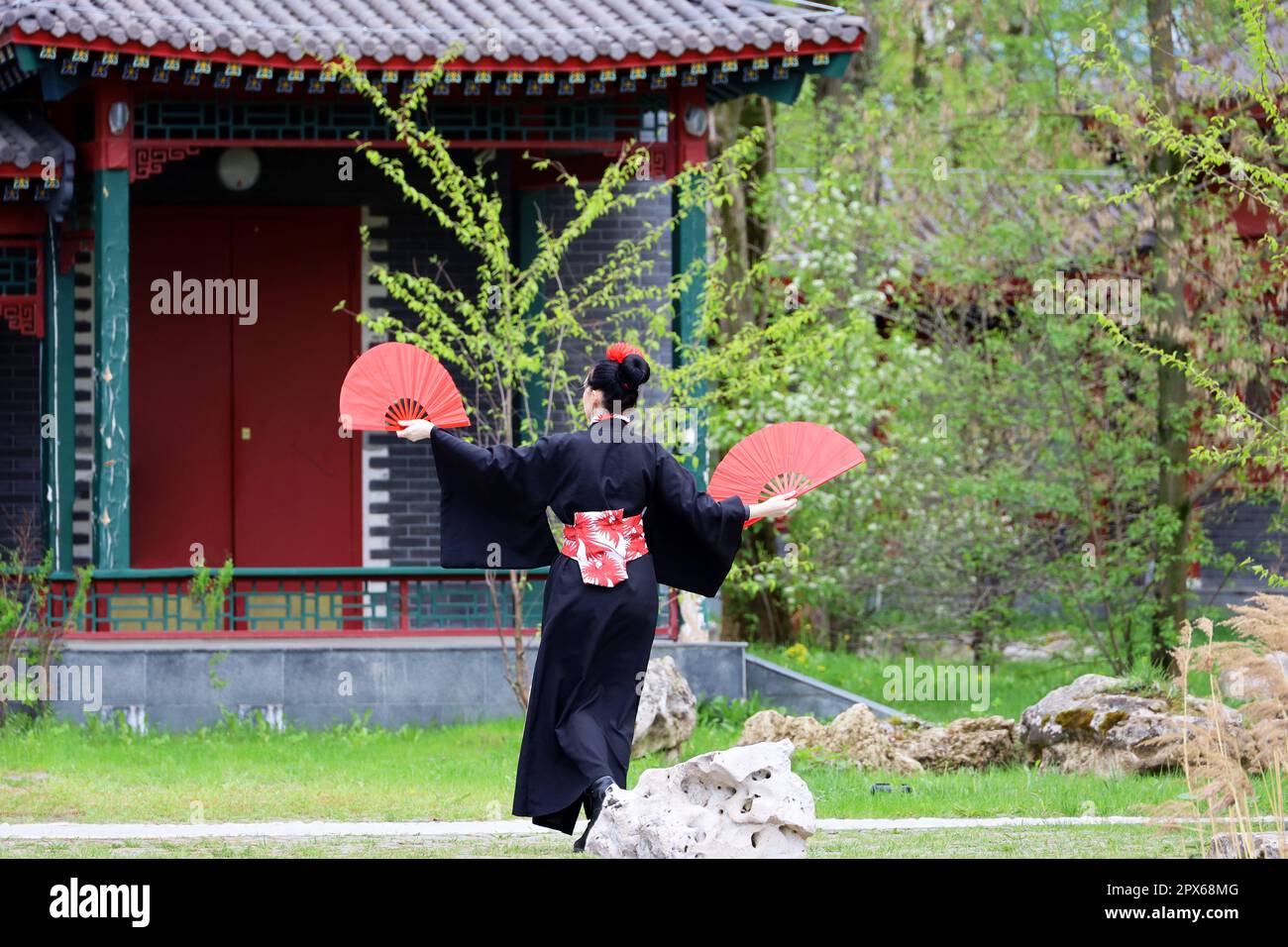 Girl in a traditional asian dress dancing in garden with fans in her hands. Asian beauty and culture Stock Photo