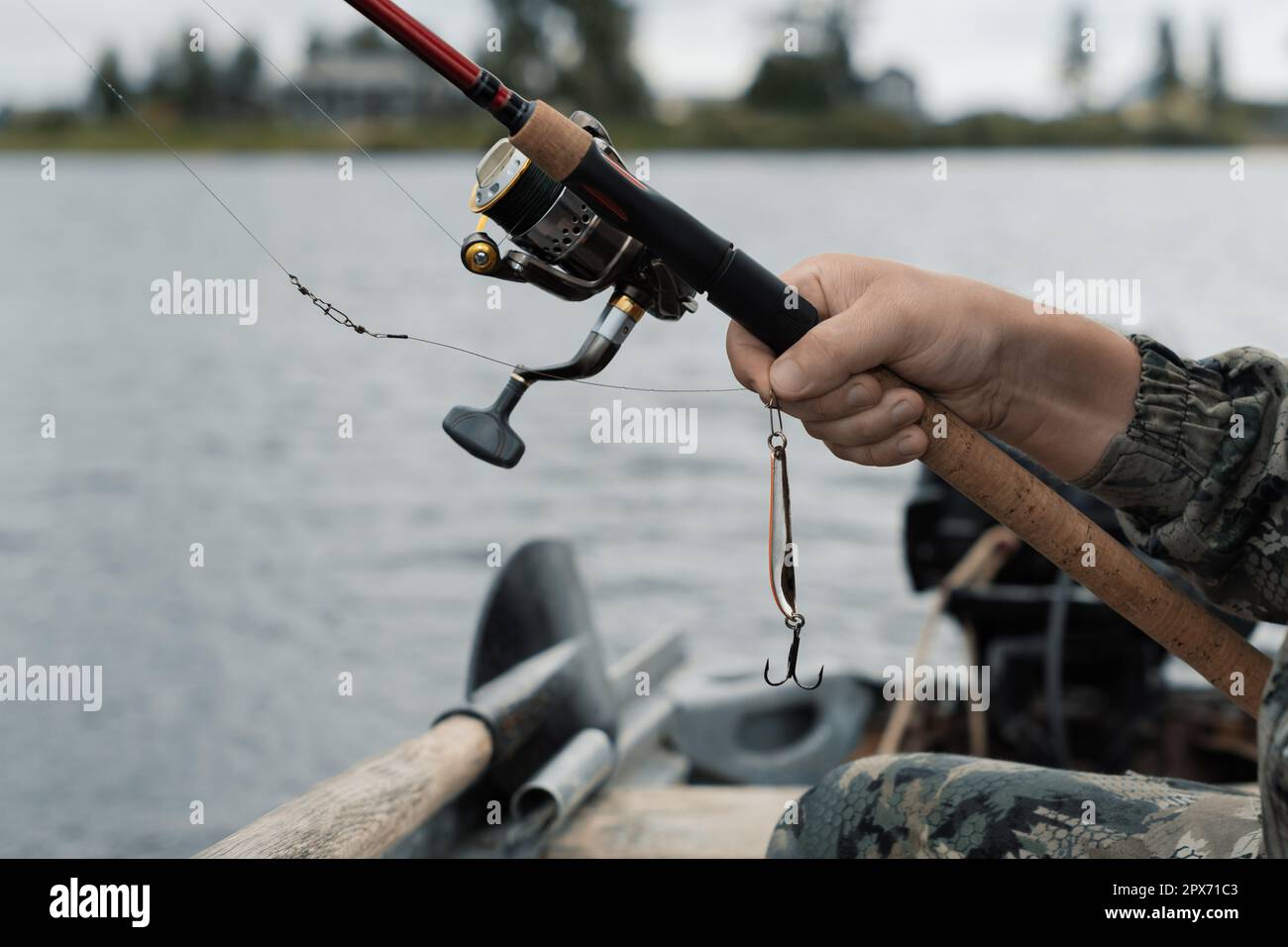 Fisherman holding spinning rod with fishing reel and fishing lure in hand in boat, close up Stock Photo