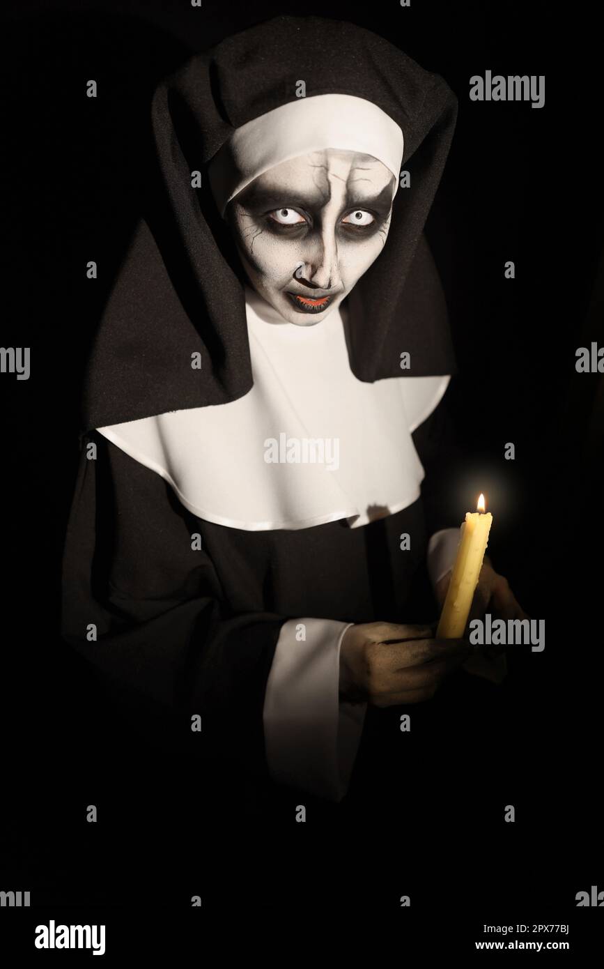 Scary devilish nun with burning candle on black background
