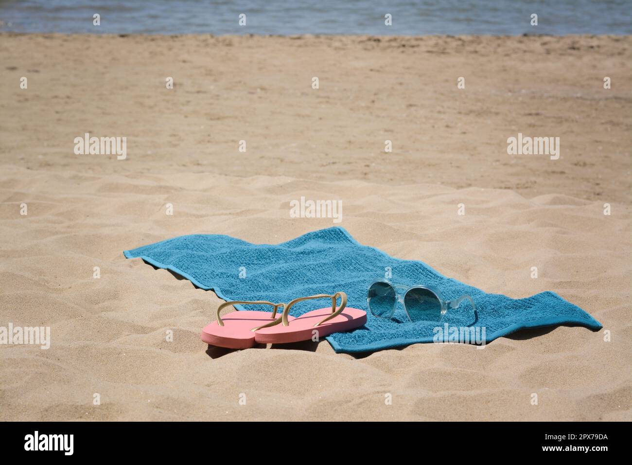 Soft blue beach towel, pink flip flops and sunglasses on sand near sea ...