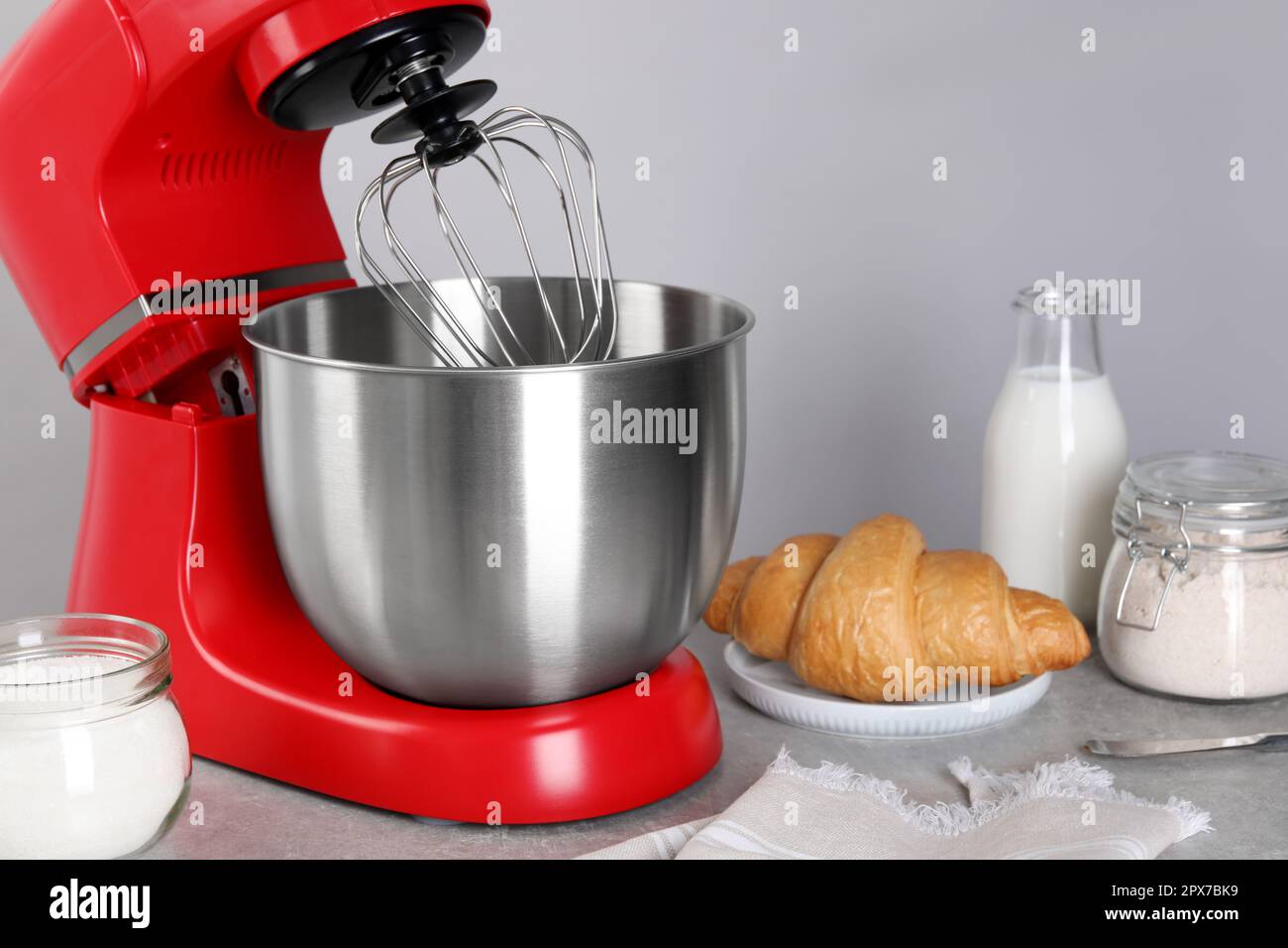 Modern red stand mixer, croissant and ingredients on gray marble table