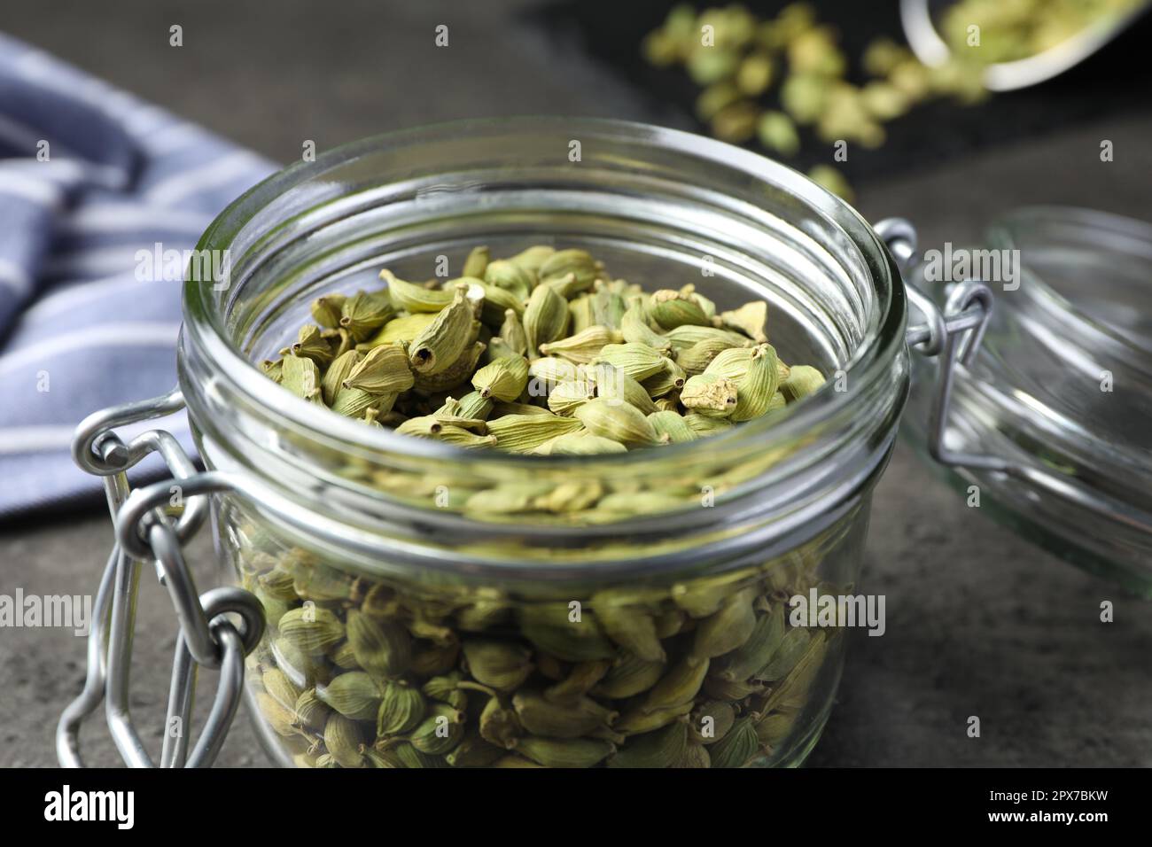 Glass jar with dry cardamom pods on dark grey table, closeup Stock