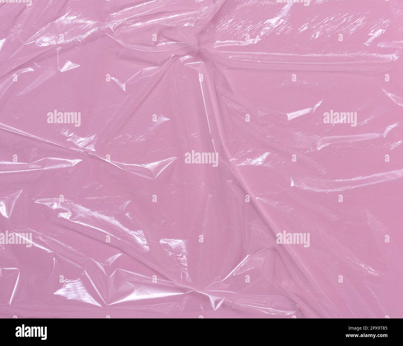 Texture of crumpled transparent polyethylene on a pink background, full frame. Stock Photo