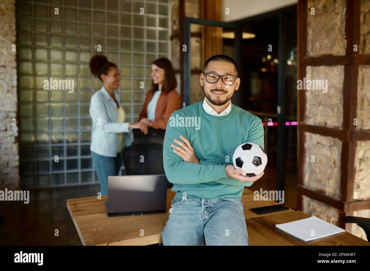 Portrait of young businessman holding soccer ball standing at coworking ...