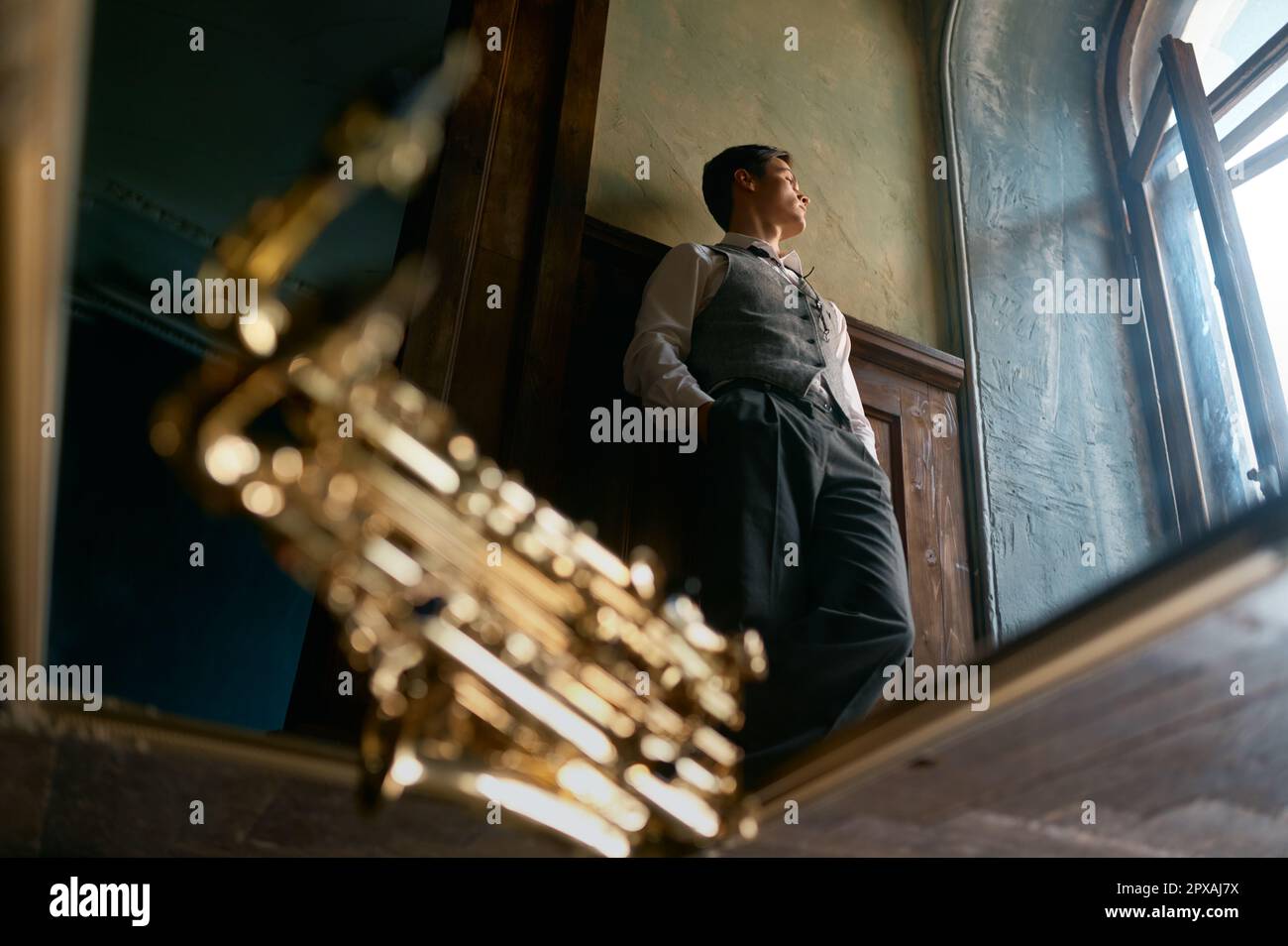 Pensive young saxophonist looking through window view from bottom, selective focus mirror reflection Stock Photo
