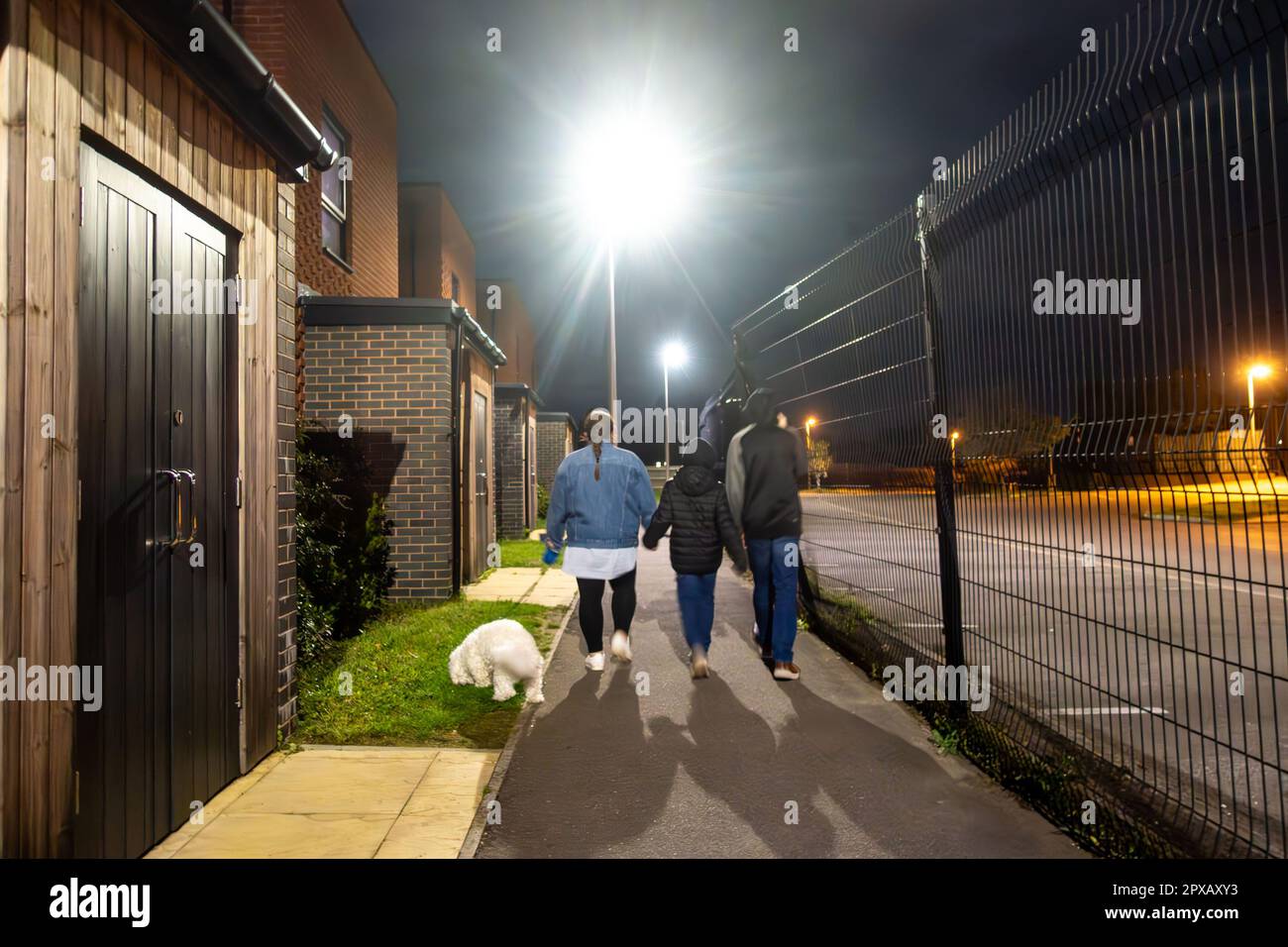 A family walk their dog late in the in the dark in the evening, walking along a footpath Stock Photo