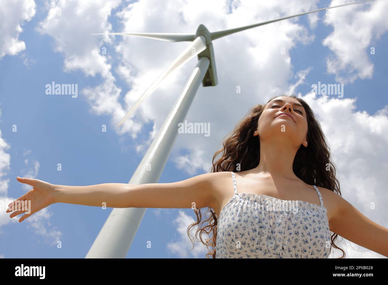 Woman outstretching arms under a windmill celebrating renewable energy
