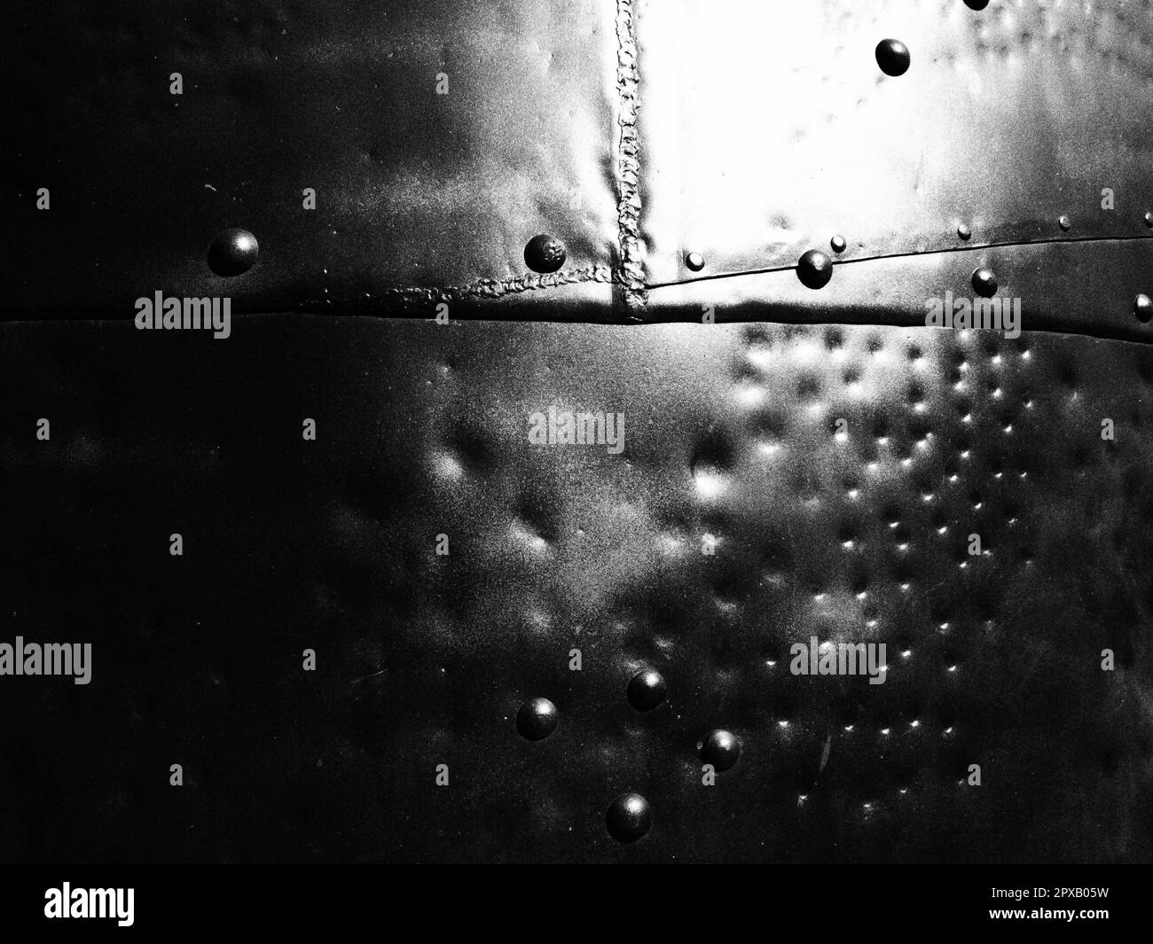 Metal surface with rivets and bolts. Abstract background of a military or industrial nature. Sheathing with dents, seams and nuts. Fasteners on metal. Stock Photo