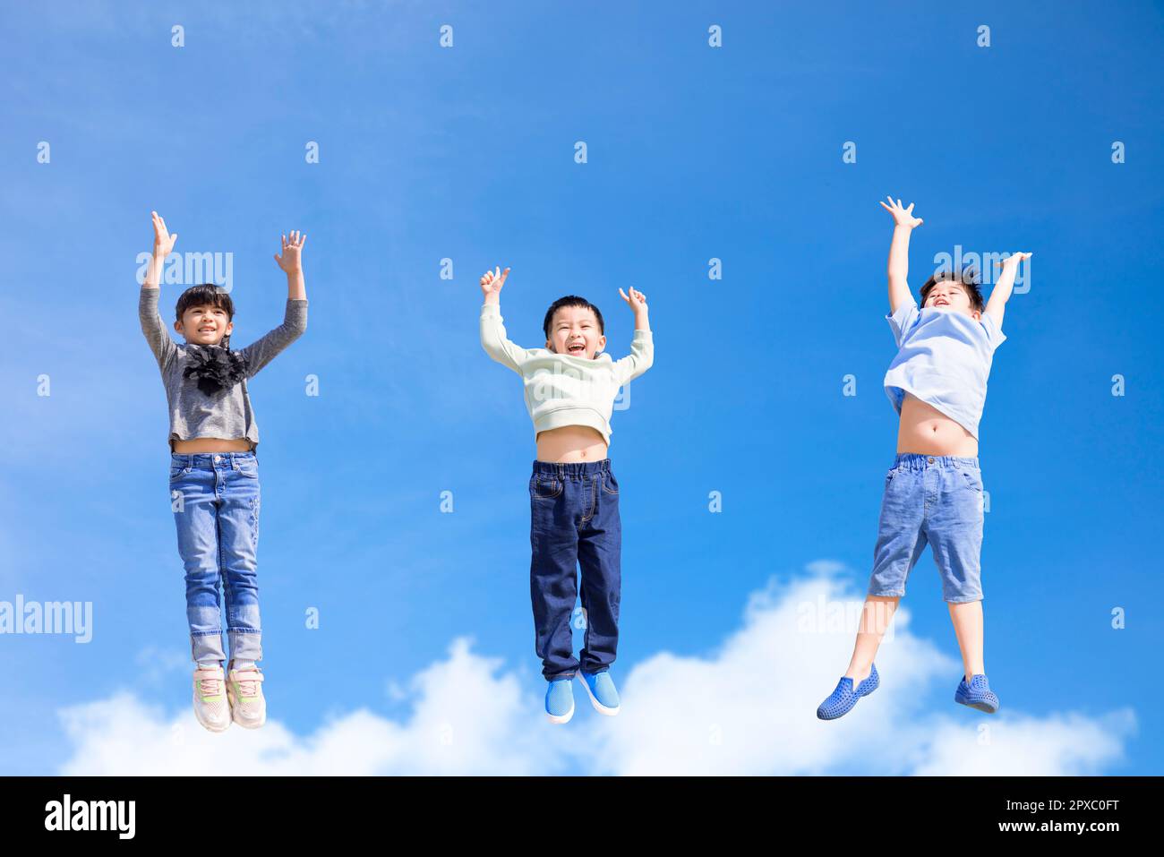 Happy kids jumping and gesturing against blue sky Stock Photo