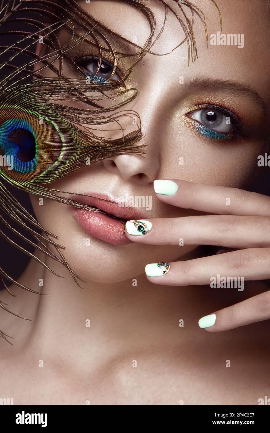Beautiful girl with bright makeup, manicure design and peacock feather