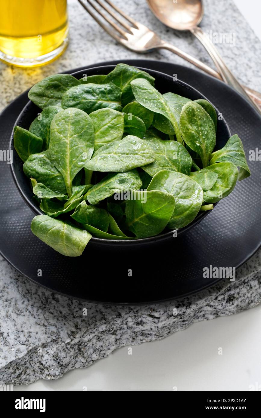 Fresh baby spinach in a black bowl and silver cutlery on a gray stone Stock Photo