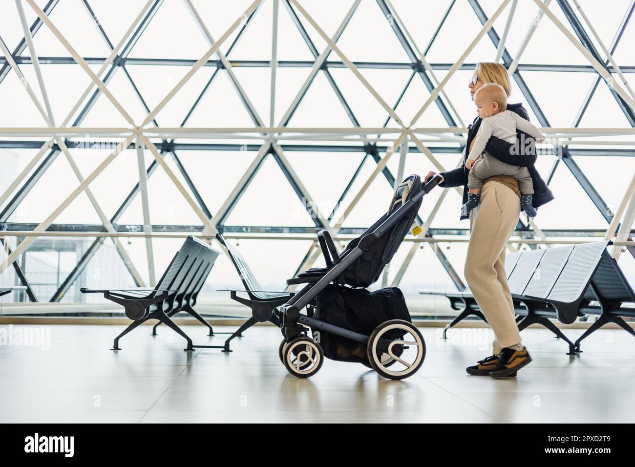 Mother carying his infant baby boy child, pushing stroller at airport