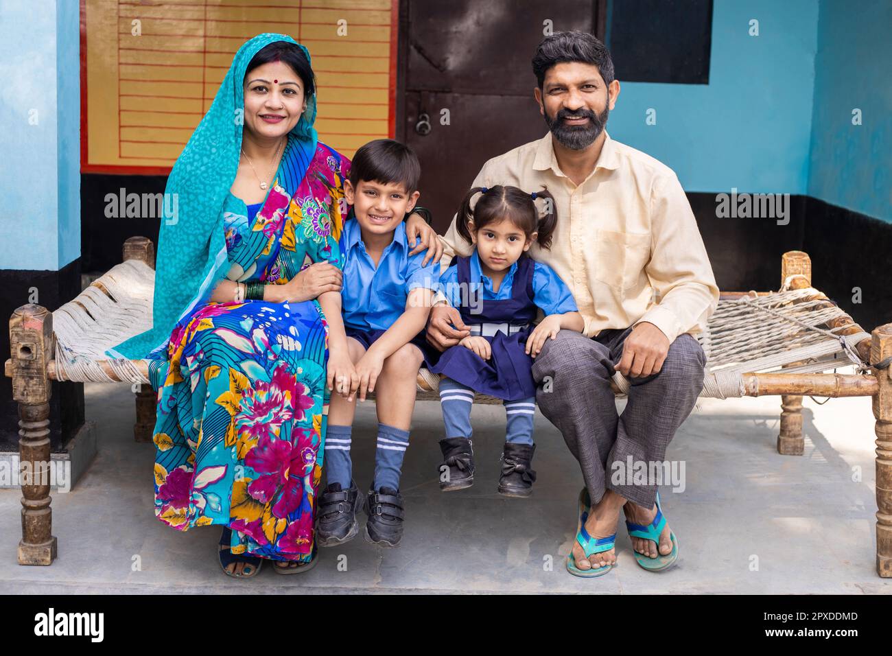 Portrait of young happy indian parents sitting with little son and daughter wearing school uniform, Rural india, Education concept. Stock Photo
