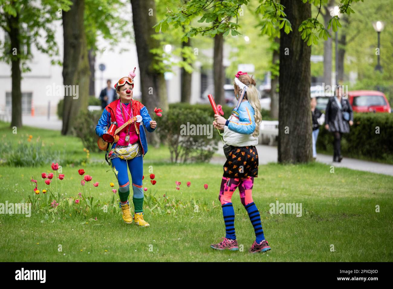 Berlin, Germany. 02nd May, 2023. Red Noses clowns Natascha (l) and Perdita Poppers run on a grassy strip on the Charité grounds at the start of the nationwide clown relay through clinics and care facilities. The association Rote Nasen Deutschland e.V. has been bringing laughter and joie de vivre to people in need for 20 years with specially trained artists. Credit: Hannes Albert/dpa/Alamy Live News Stock Photo