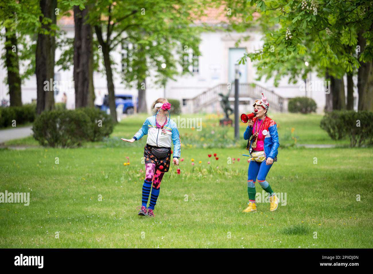 Berlin, Germany. 02nd May, 2023. Red Noses clowns Natascha (r) and Perdita Poppers run on a grassy strip on the Charité grounds at the start of the nationwide clown relay through clinics and care facilities. The association Rote Nasen Deutschland e.V. has been bringing laughter and joie de vivre to people in need for 20 years with specially trained artists. Credit: Hannes Albert/dpa/Alamy Live News Stock Photo