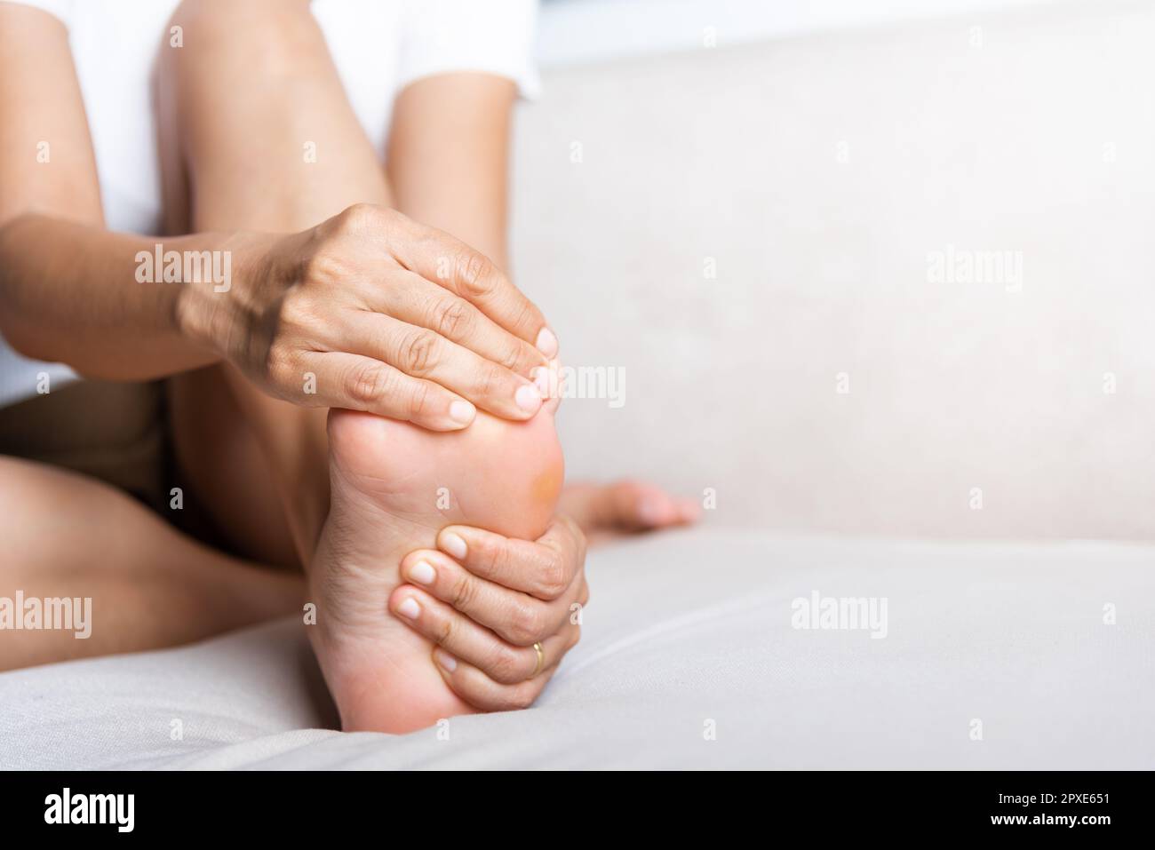 Foot pain, Asian woman sitting on sofa feeling pain in her foot at home