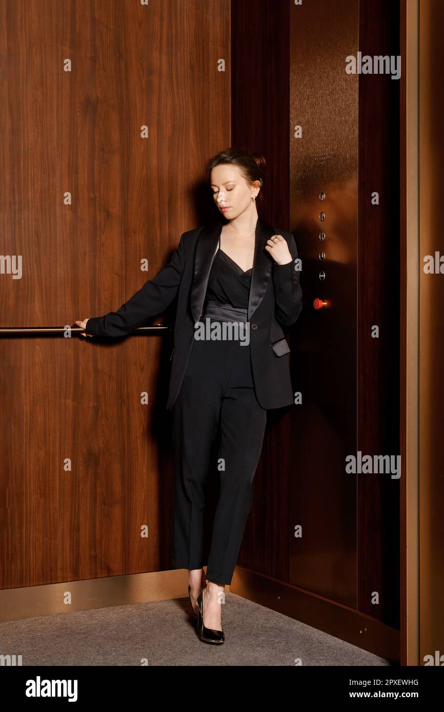 Elegant woman in black pantsuit standing in elevator and looking down Stock Photo