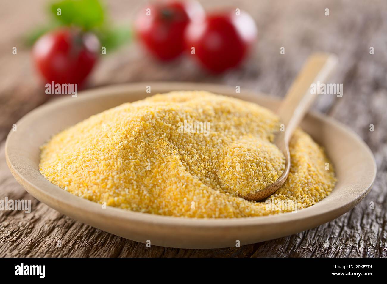 Raw coarsely ground cornmeal or polenta on wooden plate with wooden