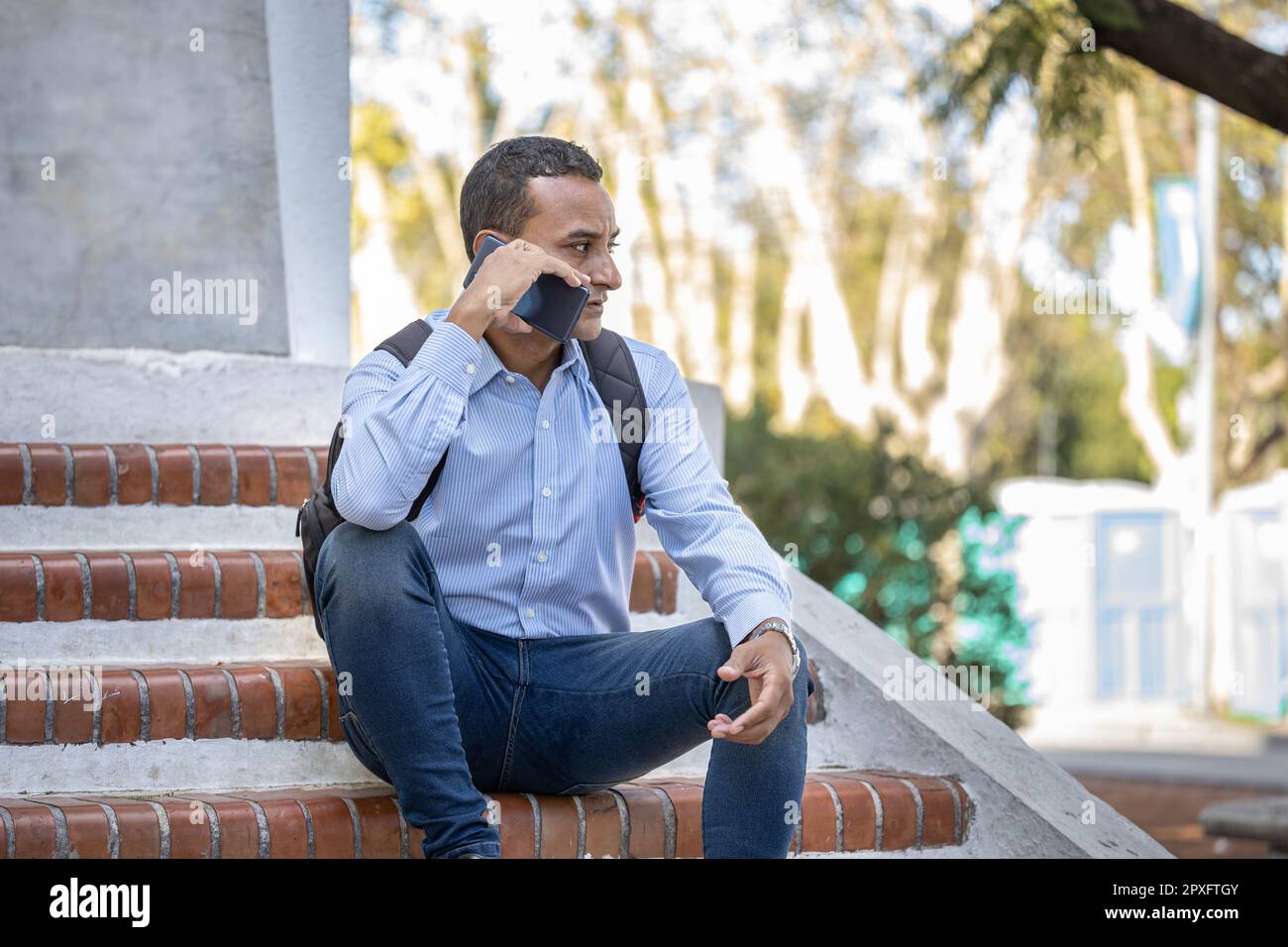 Young latino man sitting on some stairs talking on his mobile phone. Stock Photo