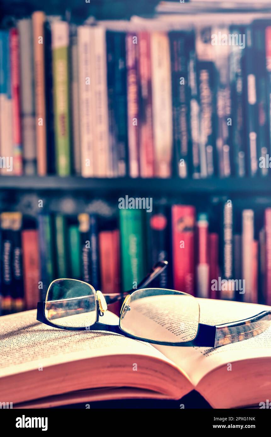 Open book and glasses with books on a shelf in the background. Theme of spending free time deepening your knowledge. Photo with a shallow depth of fie Stock Photo