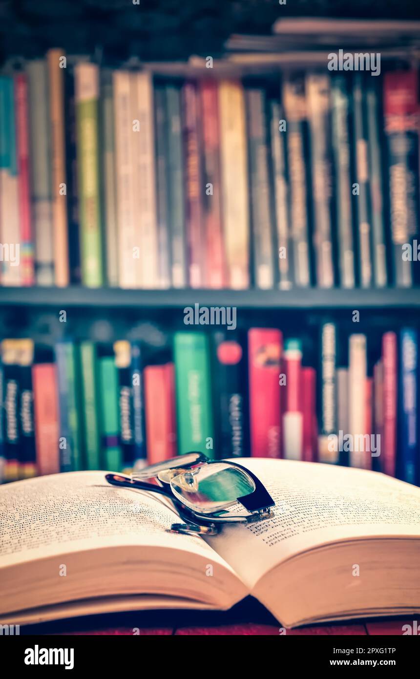 Open book and glasses with books on a shelf in the background. Theme of spending free time deepening your knowledge. Photo with a shallow depth of fie Stock Photo